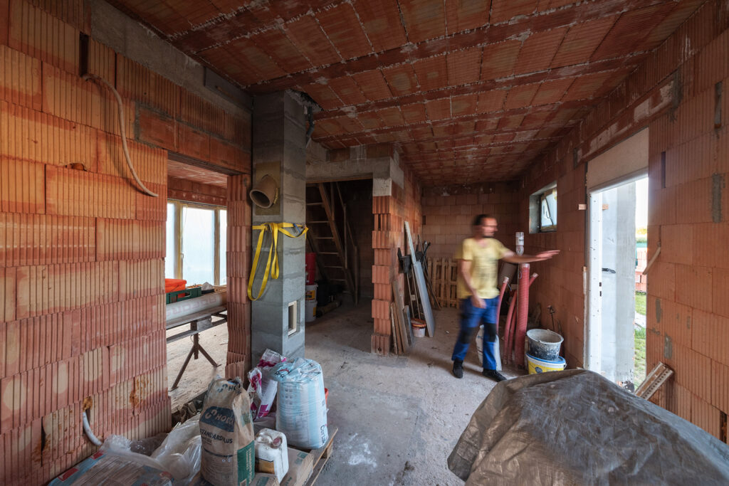 Interiér hrubé stavby domu z cihel HELUZ, pohled na strop s MIAKO vložkami a stavební materiál.