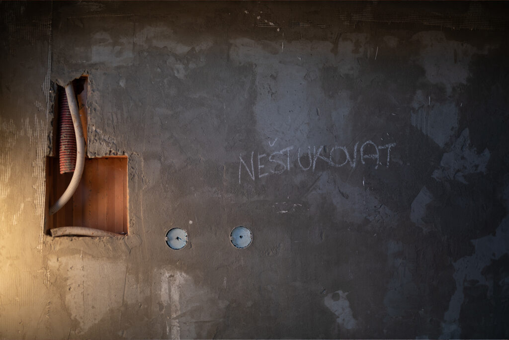 Stěna s drážkami pro elektroinstalaci ve zdivu HELUZ, nápis na omítce v hrubé stavbě.