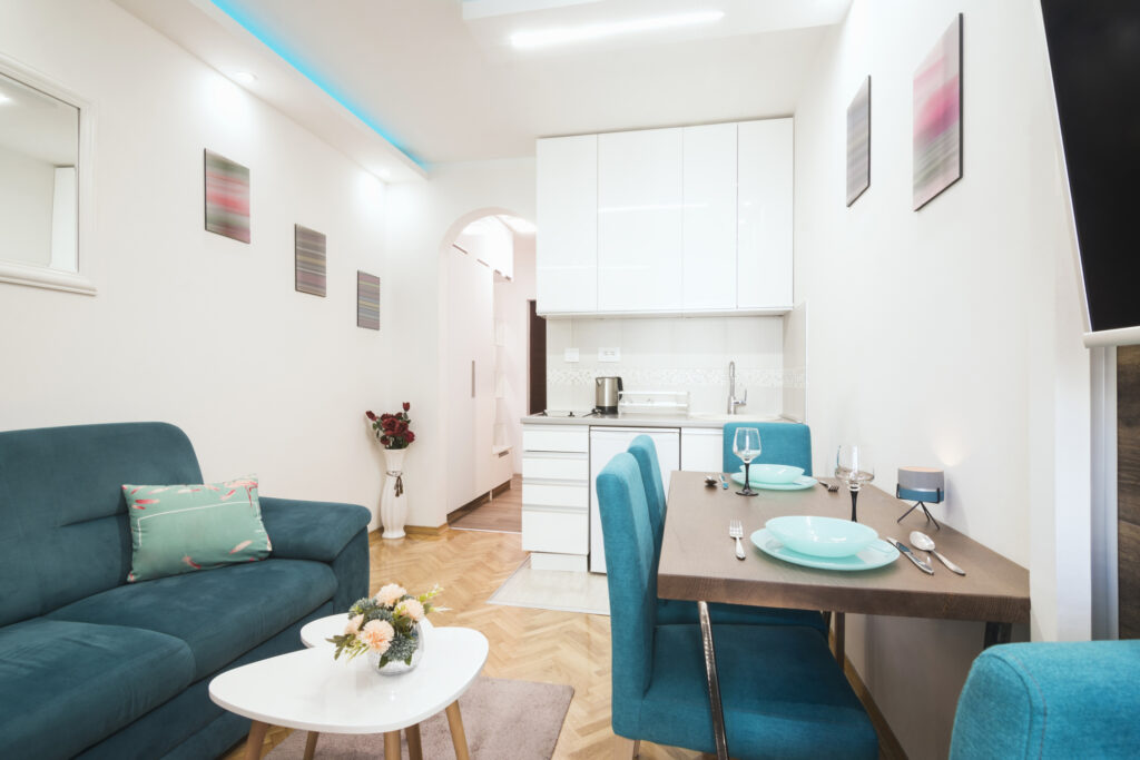 Světlý malý obývací pokoj s kuchyňským koutem, kde světlé barvy a jednoduchý nábytek pomáhají opticky zvětšit prostor